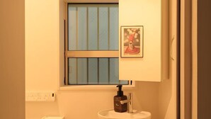 A bathroom with a white sink, a window with vertical blinds, a toilet paper dispenser, and a framed picture on the wall. - URBAN HOUSE HATAGAYA (Tokyo)