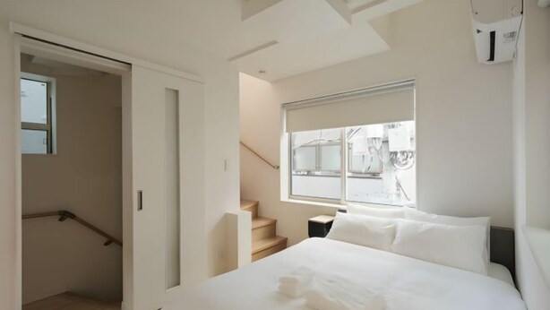 A modern hotel room with a large bed, a window with a view, and a staircase. - URBAN HOUSE HATAGAYA (Tokyo)