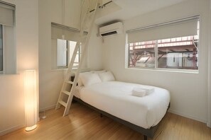 A bedroom with a bed, a ladder, a standing lamp, and a window with an air conditioning unit. - URBAN HOUSE HATAGAYA (Tokyo)