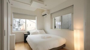 A modern bedroom with a large bed, a bedside table, a floor lamp, and a window with blinds. - URBAN HOUSE HATAGAYA (Tokyo)