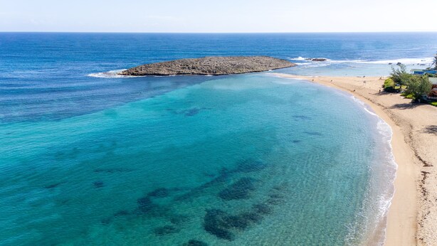 A coastal beach with clear turquoise waters, a rocky outcrop, and a sandy shore with some vegetation. - Casa Brisa del Mar – Steps to Montones Beach (Isabela)