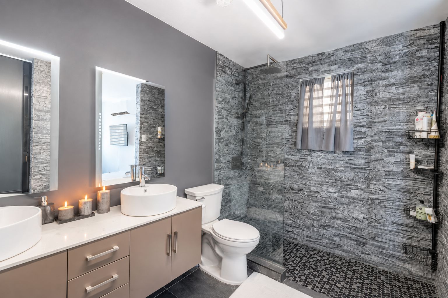 Un baño moderno con pared de textura de piedra, un lavabo redondo, un inodoro y zona de ducha.