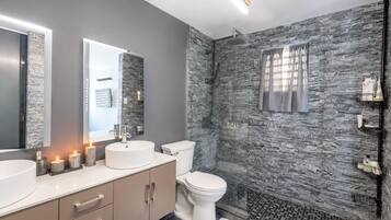 Un baño moderno con pared de textura de piedra, un lavabo redondo, un inodoro y zona de ducha.