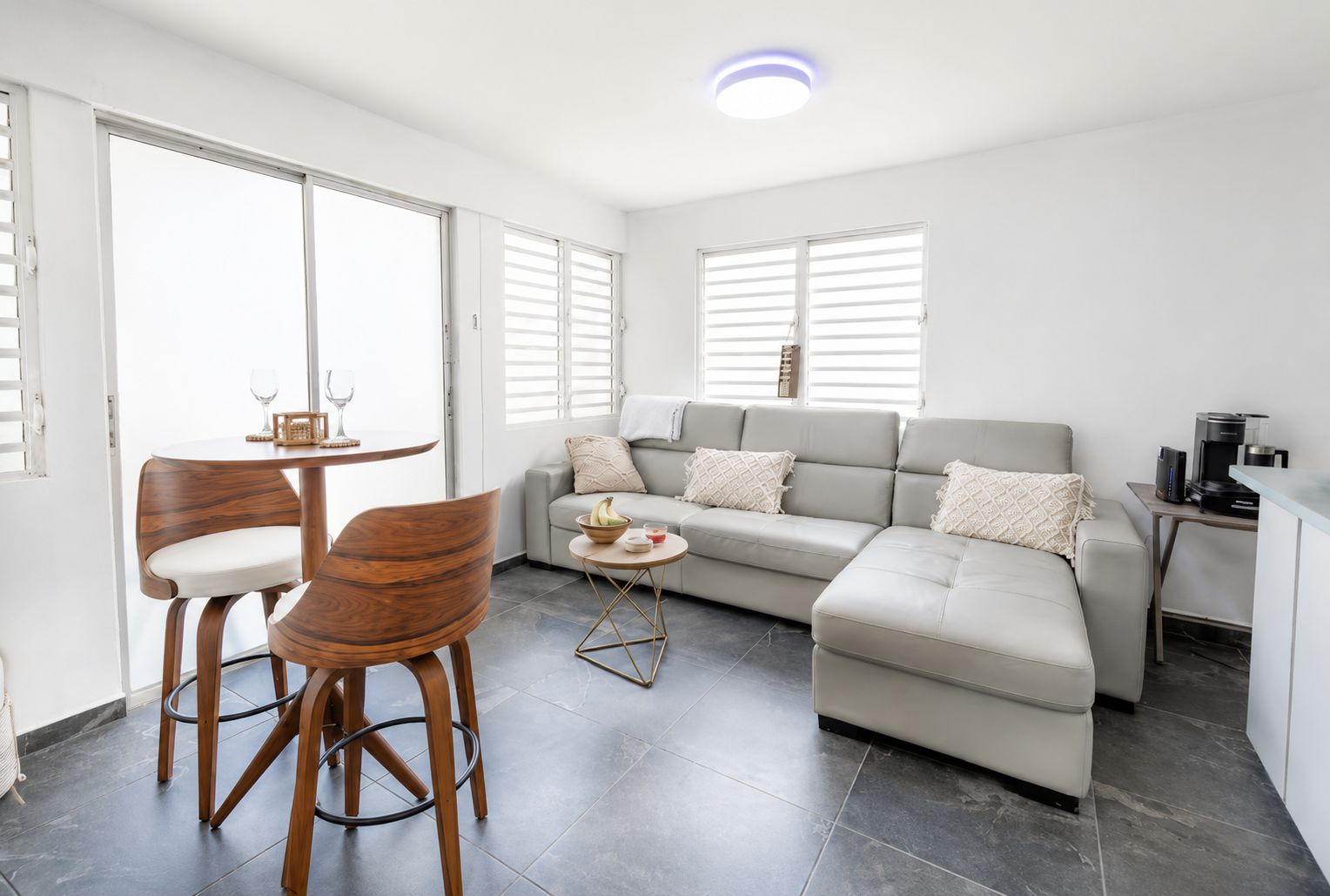 A modern living room with a sofa, two wooden chairs, a coffee table, and a dining table.
