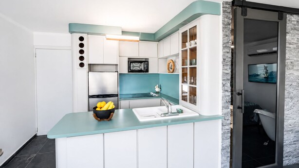 A compact kitchen with white cabinets, a teal countertop, and a built-in microwave.