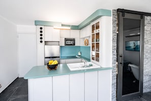 Una cocina compacta con armarios blancos, encimera verde azulado y microondas integrado.