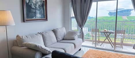 A living room with a sofa, a chair, a lamp, and a large window with a view of a building and greenery.