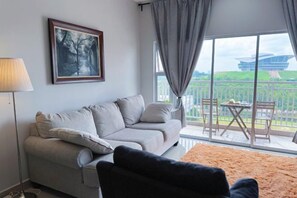 A living room with a sofa, a chair, a lamp, and a large window with a view of a building and greenery. - PPAM Seruling Presint 5, Putrajaya 4BR+ PICC View (Putrajaya)