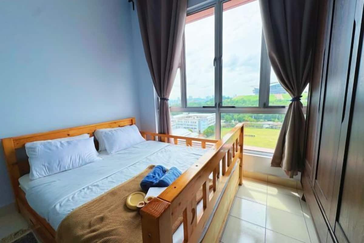 Un dormitorio con cama de madera, ventana con cortinas y vistas a zonas verdes y edificios.