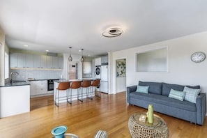 A modern kitchen with bar stools, a dining area with a sofa, and a living room with a coffee table. - Serene 2BR Home in Meadowbank w Balcony & Parking (Auckland)