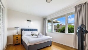 Ein Schlafzimmer mit Bett, Nachttisch, Lampe, Fenster und Ventilator.