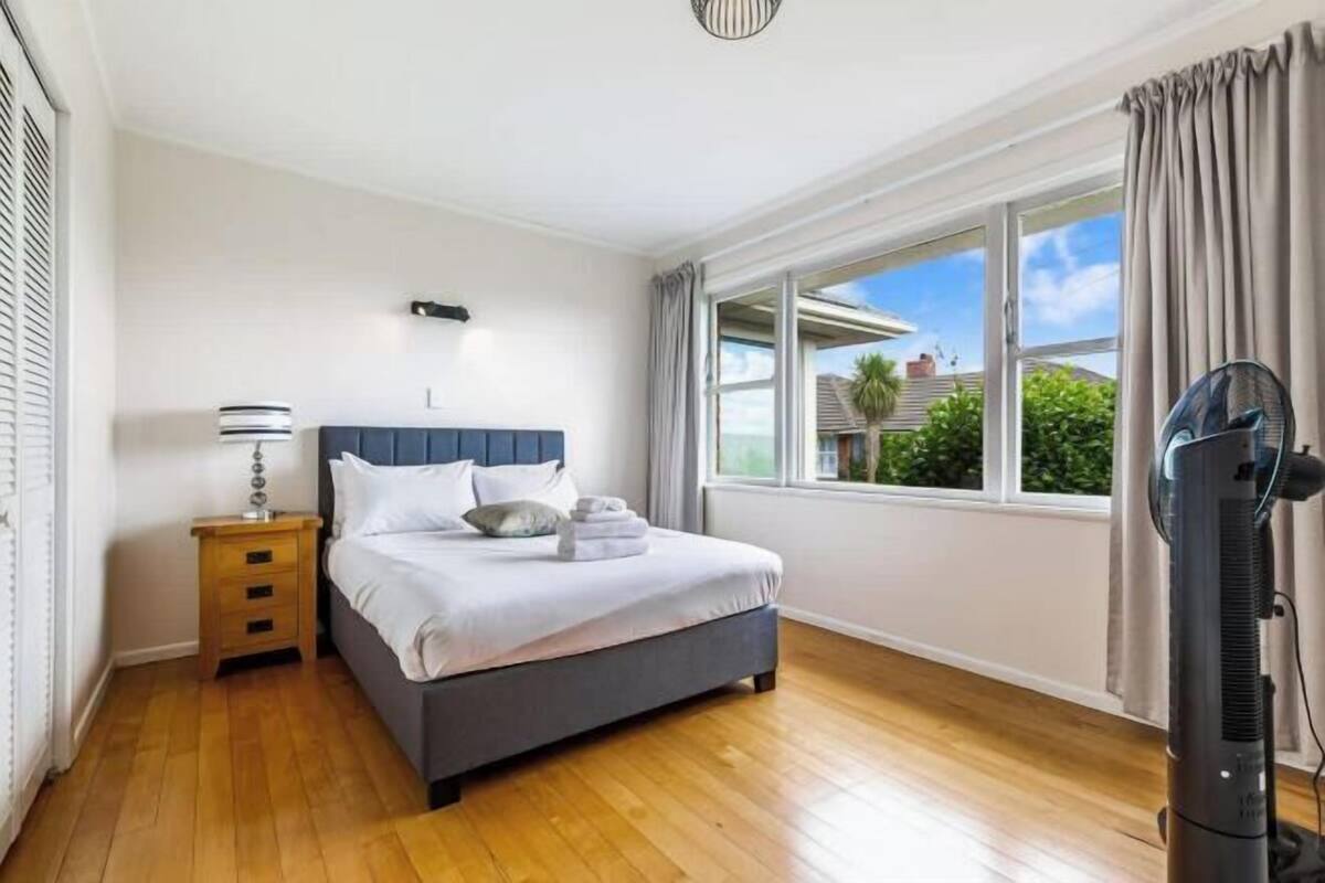 Un dormitorio con cama, mesita de noche, lámpara, ventana y ventilador.