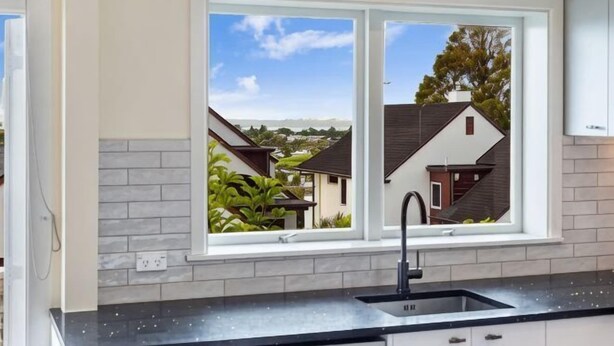 Eine Küche mit Fenster, Spüle und Blick auf benachbarte Häuser.