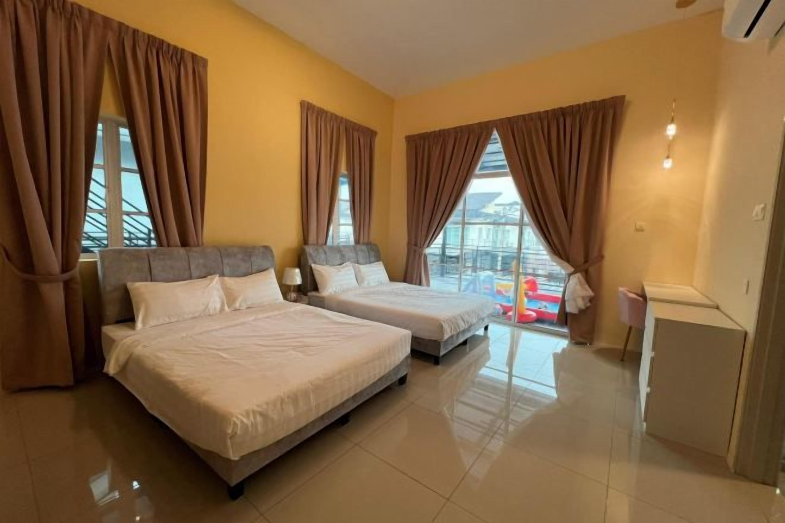 Habitación de hotel con dos camas, ventanas amplias con cortinas, vista a un balcón y un escritorio pequeño con lámpara.