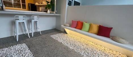 A modern interior with a bar area, seating with colorful cushions, and a pebble-patterned floor.