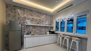 Eine moderne Küche mit Musterfliesen, weißen Schränken, einem Kühlschrank und Barhocker an einem Fenster.