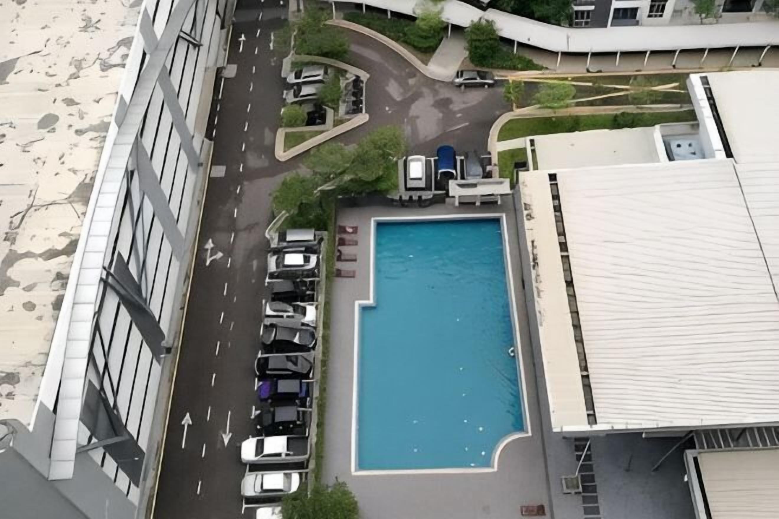 An aerial view of a building with a swimming pool, parking lot, and a road.
