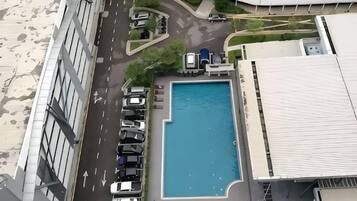 An aerial view of a building with a swimming pool, parking lot, and a road.