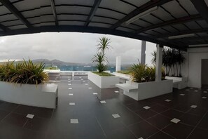 Eine offene Terrasse mit Blick auf das Meer und die Berge, mit weißen Pflanzkästen und Pflanzen sowie einem gefliesten Boden.