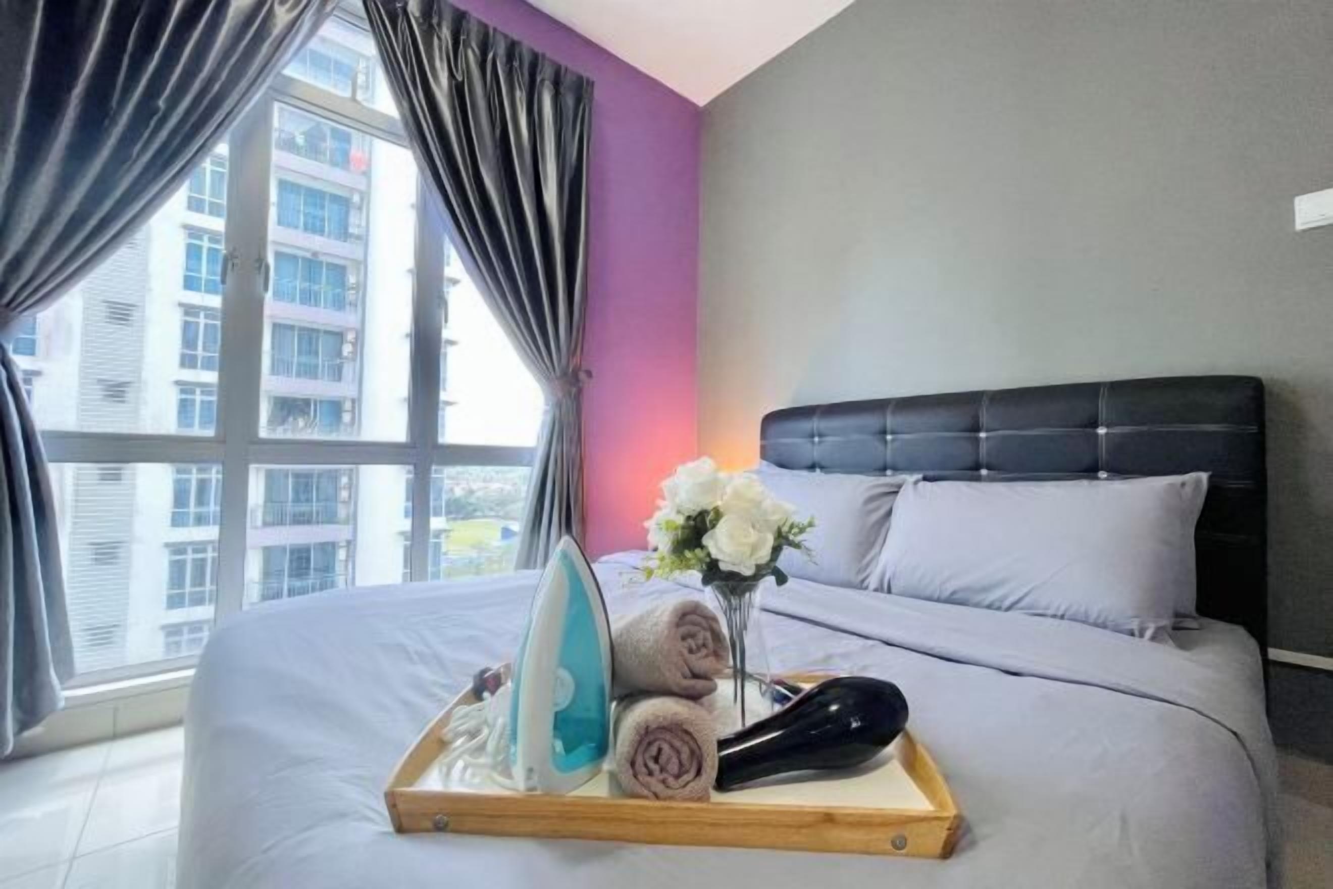 A hotel room with a bed, a tray with an iron, towels, and a vase of flowers.
