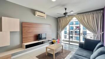A modern living room with a sofa, a coffee table, a TV on a wooden stand, and a large window with curtains.