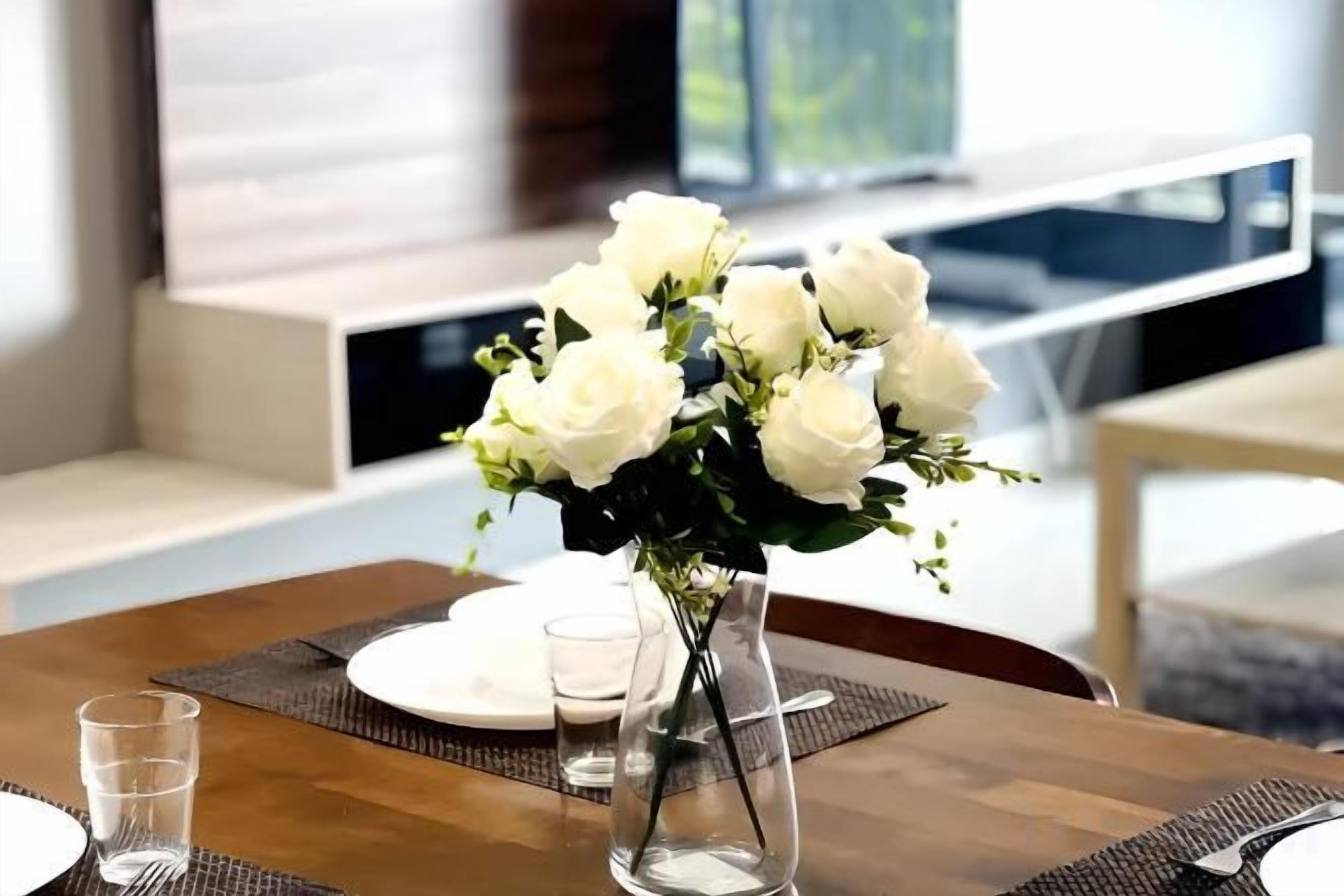 Een eettafel met een vaas witte bloemen, borden en glazen.