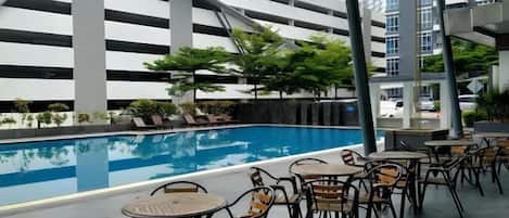 A rooftop pool area with lounge chairs and tables, surrounded by high-rise buildings.
