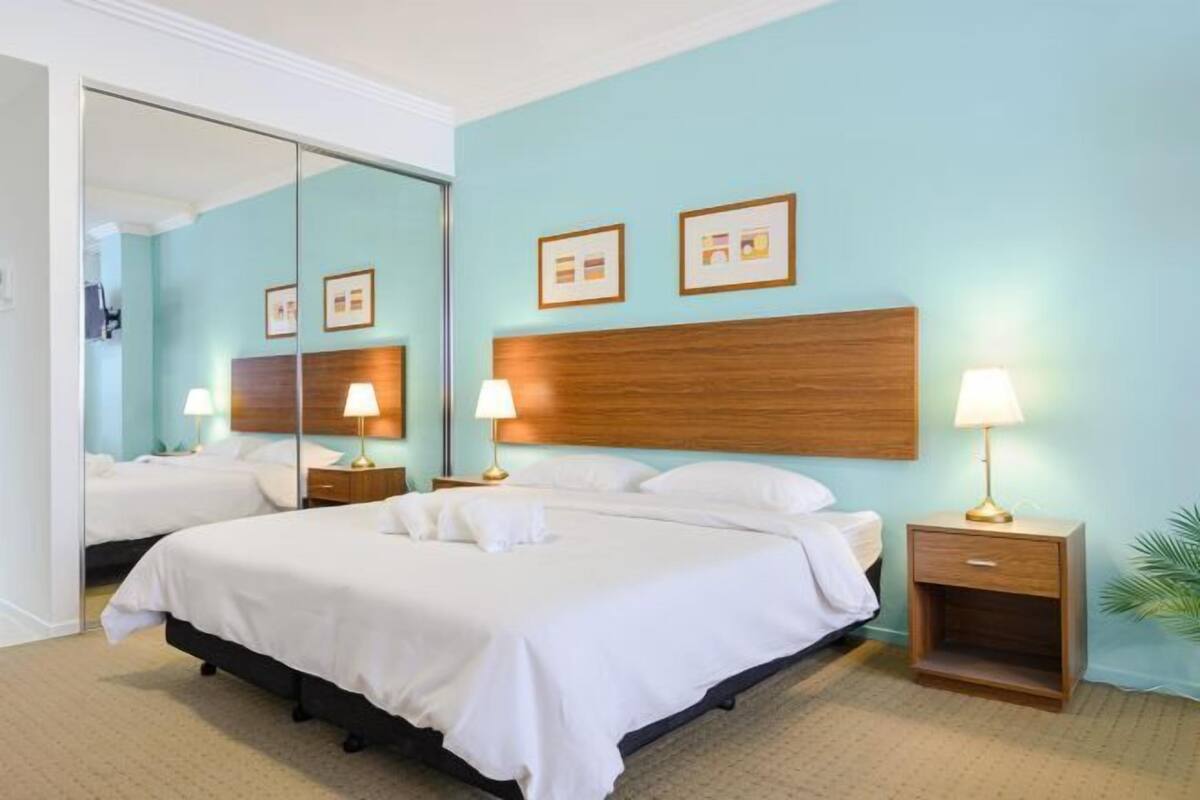 Een hotelkamer met een groot bed, twee nachtkastjes met lampen, een houten hoofdbord en een grote spiegel.