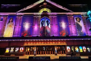 Un bâtiment orné de grandes banderoles faisant la publicité du film « La Belle et la Bête » et d’un auvent avec des lettres illuminées.
