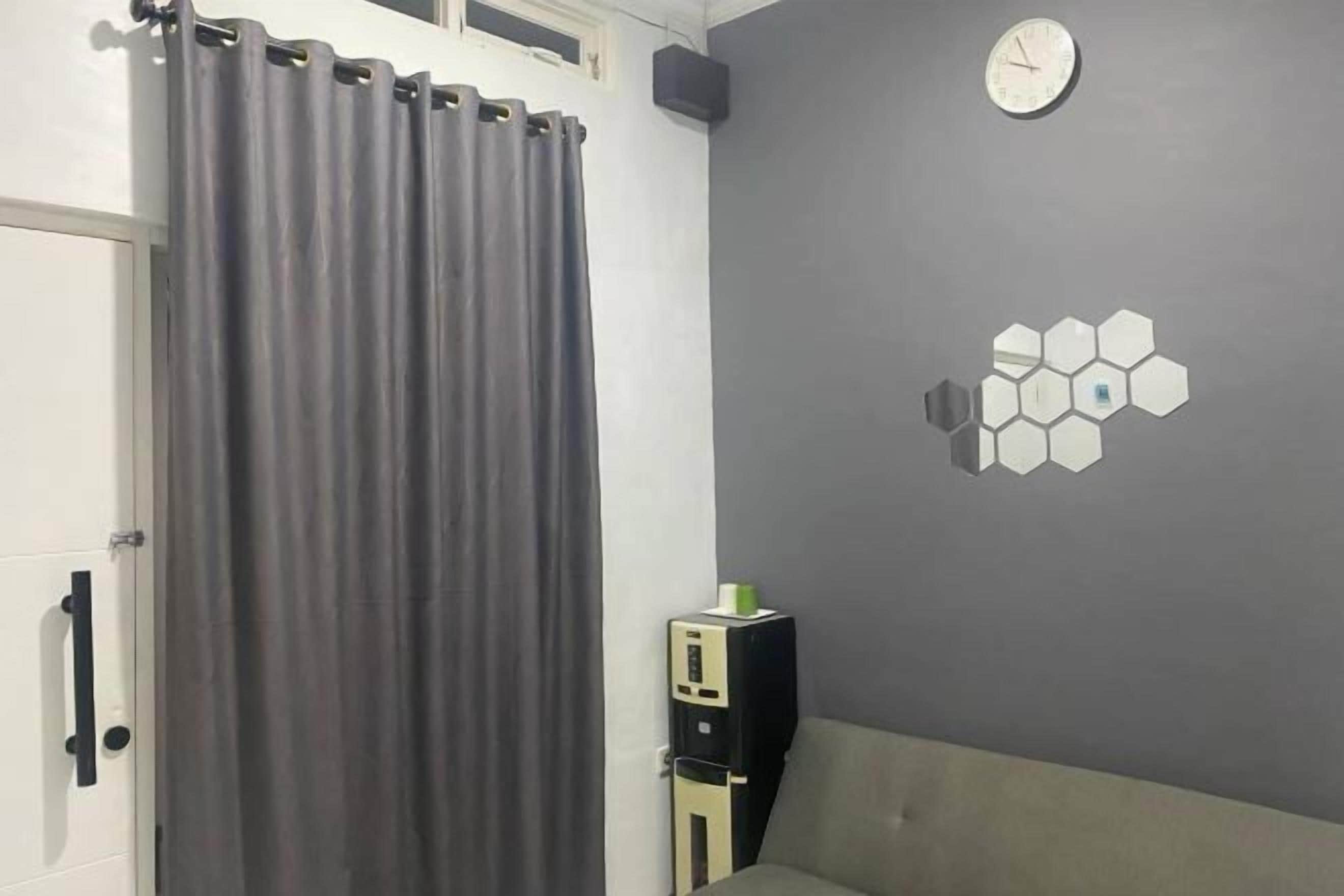 A room with a grey curtain, a white door, a grey wall with a hexagonal light fixture, and a clock.