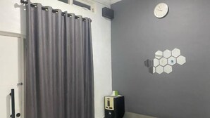 Una stanza con una tenda grigia, una porta bianca, una parete grigia con un lampadario esagonale e un orologio.
