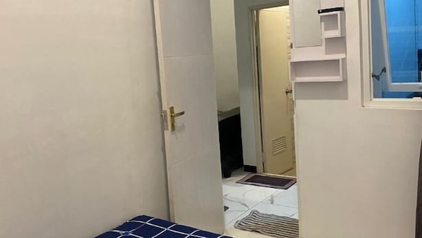 Un corridoio stretto con una porta che dà su una stanza. Sul lato destro della porta si trova una piccola finestra, e sopra di essa un mobiletto bianco.