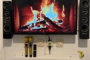 A television mounted on a wall with a fireplace image displayed, flanked by two speakers. - Yuriti Modern Minimalis Villa (Batu Sub-District)