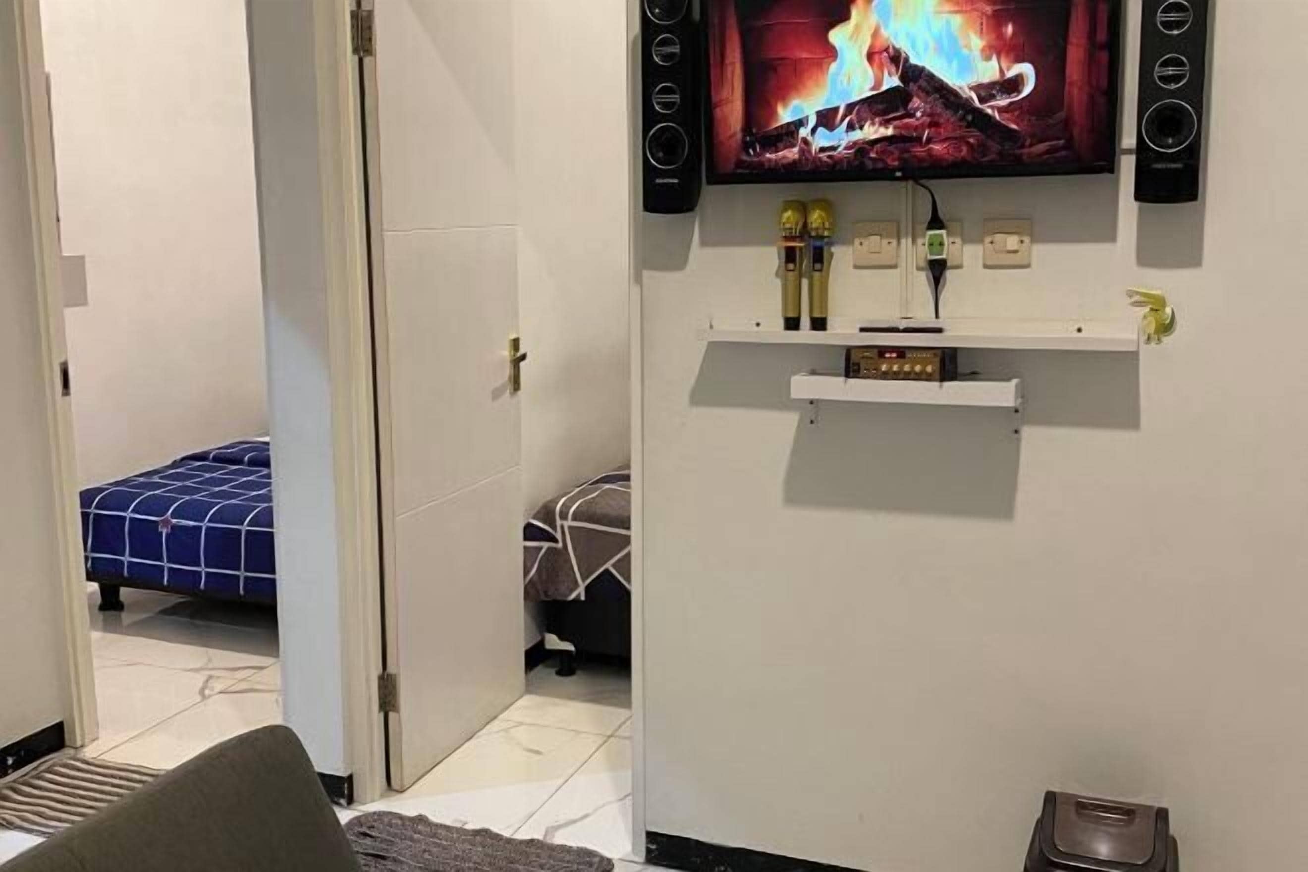 A hotel room with a bed, a TV mounted on the wall, and a small shelf with items.