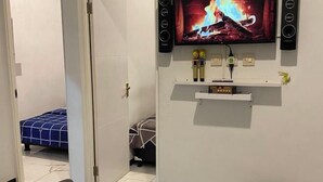 Camera d'albergo con un letto, una TV a muro e un piccolo ripiano con oggetti.