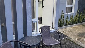 Un edificio moderno con ingresso tramite porta in vetro, due sedie in vimini e un tavolinoino all'esterno.