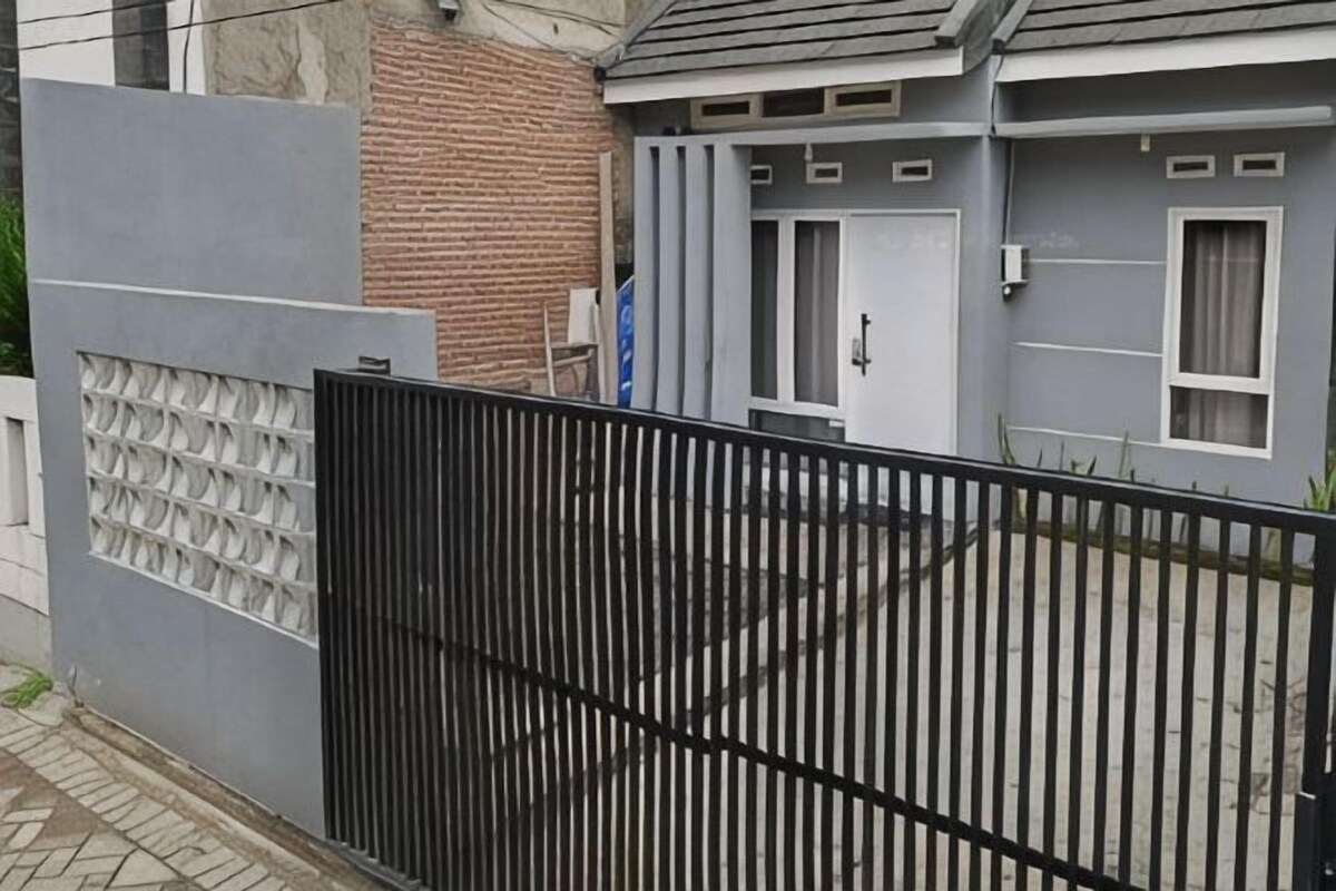 A gated residential area with a grey house, a brick wall, and a black metal fence.