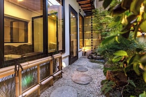 A pathway with stepping stones leading to a building with large glass doors and a bamboo fence. - Shukuhonjin Gamo (Osaka)