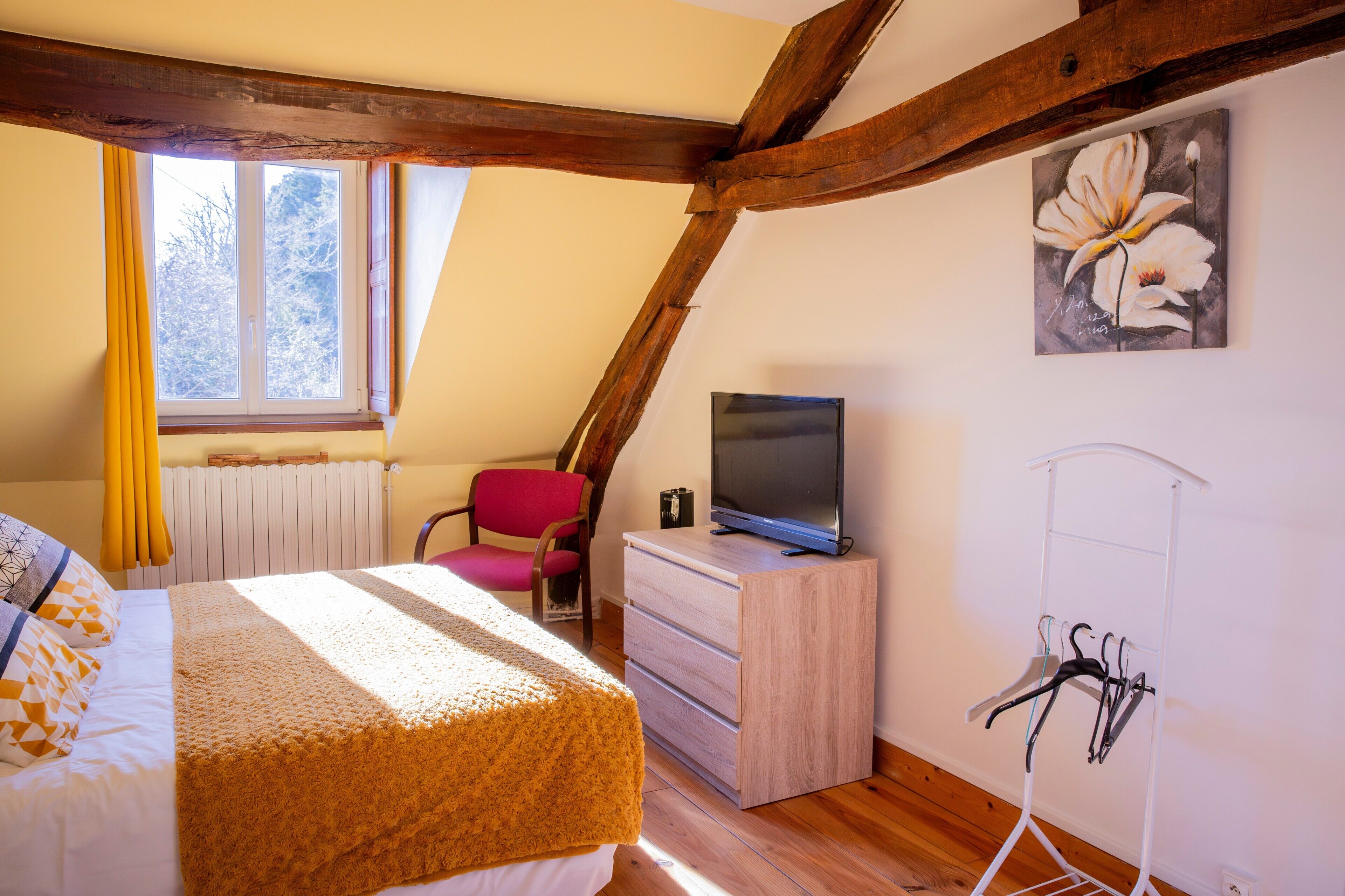 A bedroom with a bed, a dresser, a TV, a chair, and a coat rack.