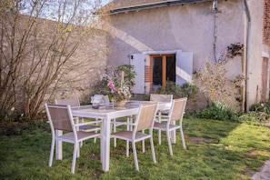 Ein weißer Tisch mit vier Stühlen in einem Gartenbereich mit einer Steinmauer und einer Holztür.