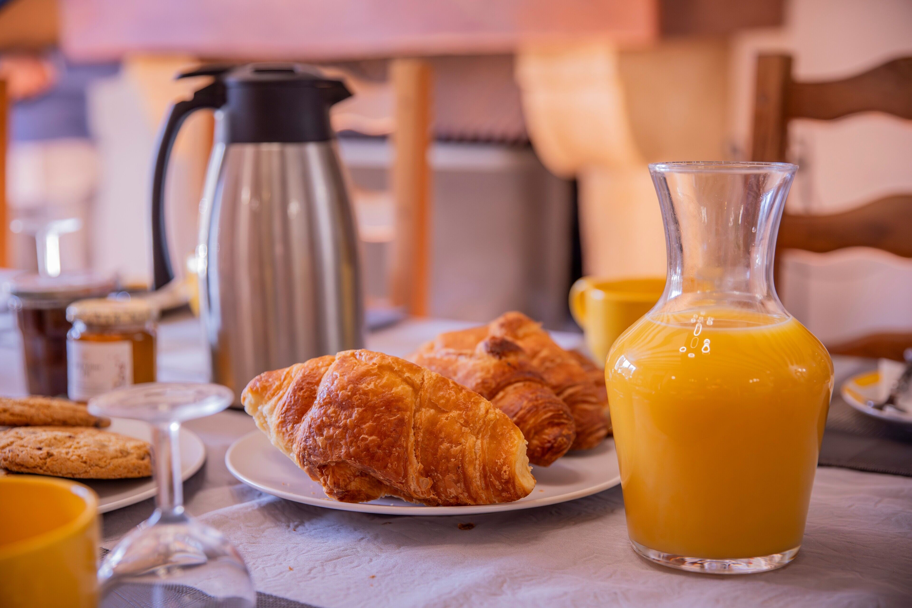 En morgenmadsopsætning med croissanter, appelsinjuice og en kaffekande.