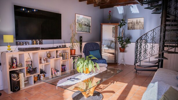 Una sala de estar con televisor, estanterías, una mesa de centro de vidrio y una escalera.
