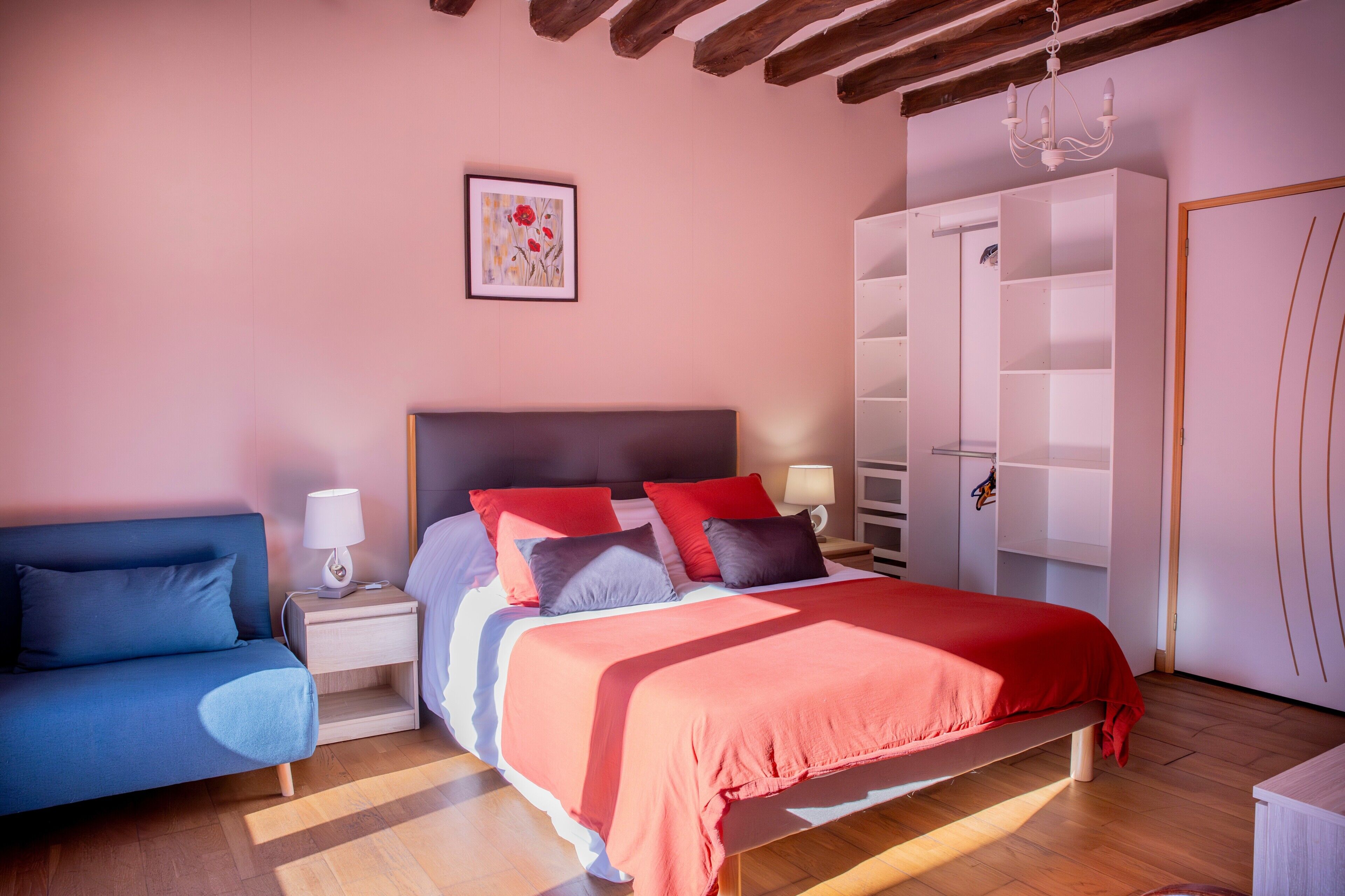 Une chambre à coucher avec un lit, une table de chevet, une lampe, une armoire et un canapé bleu.