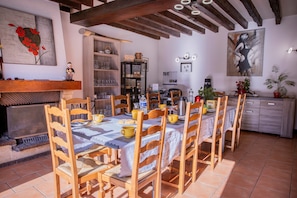 Un espace repas comprenant une longue table, des chaises, une cheminée, une bibliothèque et un coin cuisine.