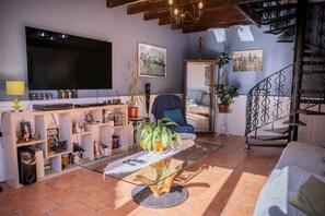 A living room with a TV, shelving, a glass coffee table, and a staircase. - Suite Bleuet - Le Petit Puits Guest Room with Shared Garden and Wi-Fi (Cheverny)