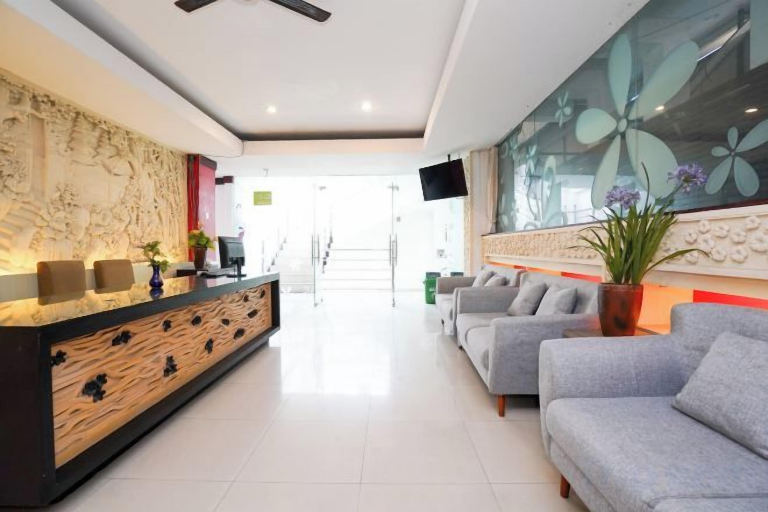 A hotel reception area with a reception desk, seating area, and a television screen.