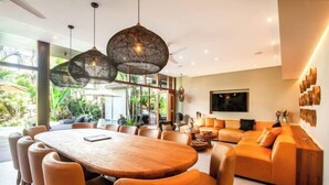 A modern dining area with a wooden table and chairs, a sofa, and pendant lighting. - Villa Na (Bali)