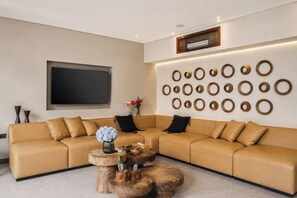 A modern living room with a beige sectional sofa, a round coffee table, and a wall-mounted circular design. - Villa Na (Bali)