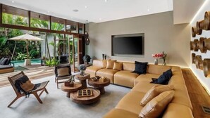 A modern living room with a large sofa, round coffee tables, and a TV mounted on the wall. - Villa Na (Bali)