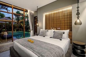 A modern bedroom with a large bed, a view of a swimming pool, and a wooden headboard. - Villa Na (Bali)